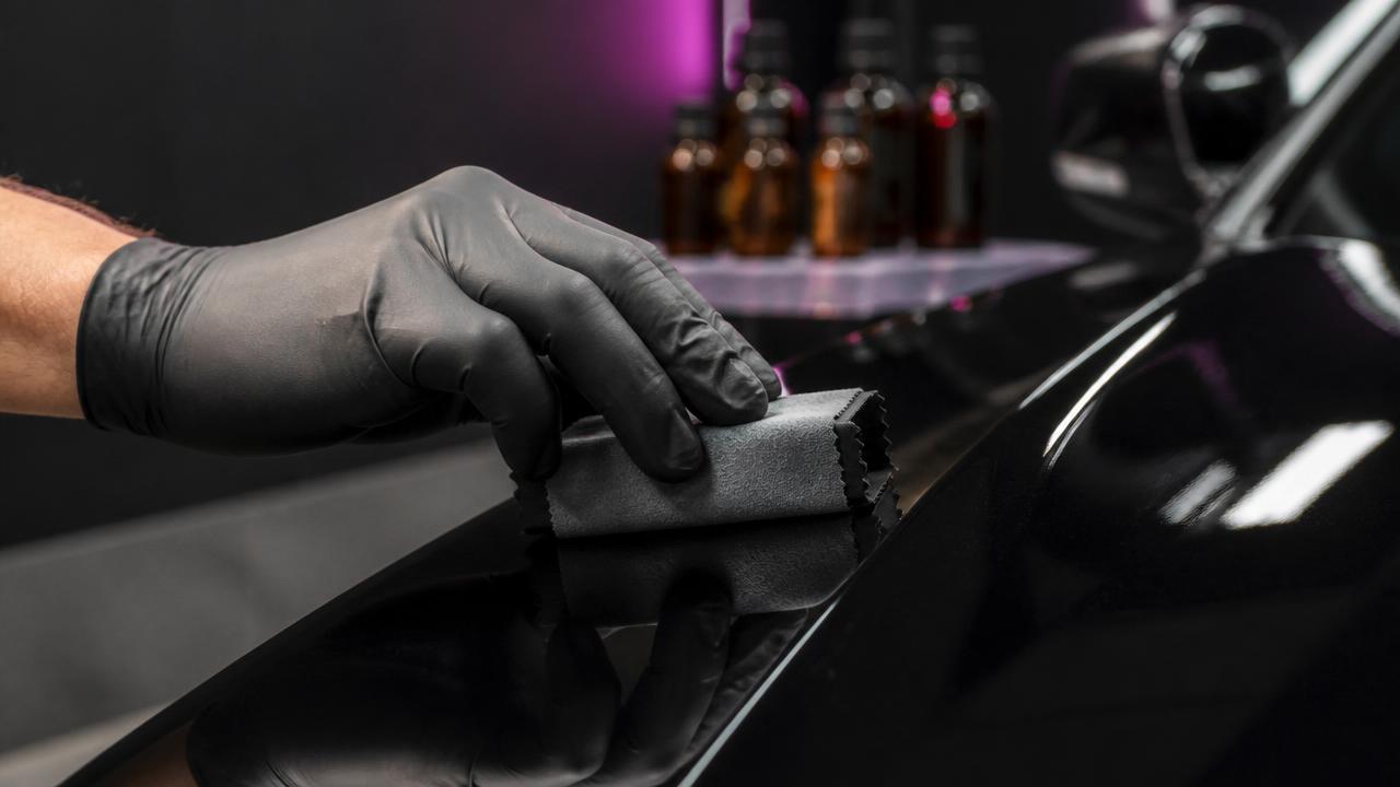 Gloved hands applying certified ceramic coating with an applicator block to a black exotic car fender